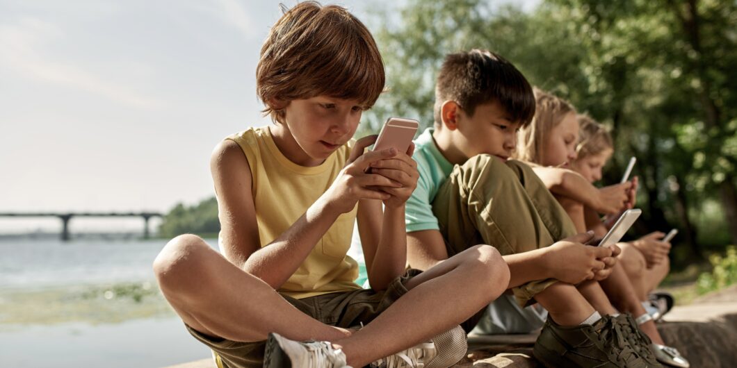 Row,Of,Multiethnic,Children,Using,And,Browsing,Mobile,Phones,On