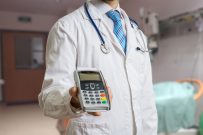 Doctor is holding payment terminal in hands. Paying for health care.