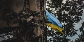 A,Ukrainian,Flag,Waves,In,The,Background,Of,War-torn,Ruins,